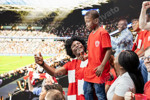 Preview: Proud Black father lifting young son in football jersey during live soccer match
