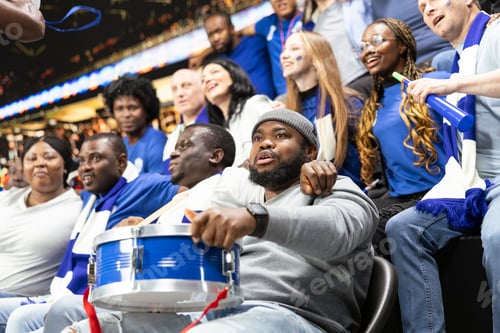 Preview: Diverse blue football fans gathered in supporter section with drum