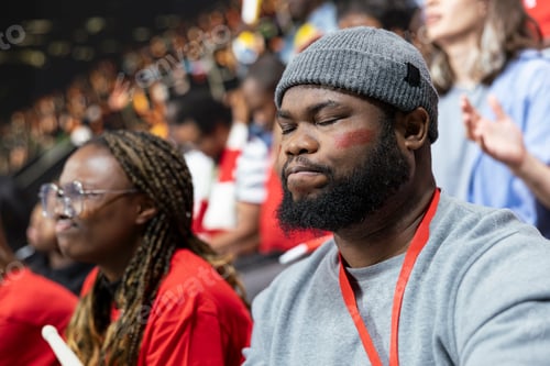 Preview: Black football fan with eyes closed holding breath in stadium stands