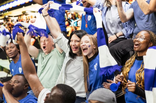 Preview: Passionate blue women supporters cheering with raised arms in stadium stands