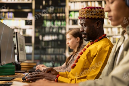 Preview: African man student working at desktop computer and wearing traditional clothes