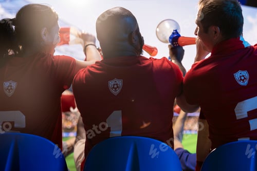 Preview: Back view of soccer fans singing with vuvuzelas in stadium, rooting for team