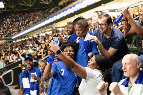 Preview: Happy soccer fans taking selfie with child during live match in crowded stadium