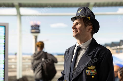 Preview: Smiling pilot captain in uniform at airport terminal window view