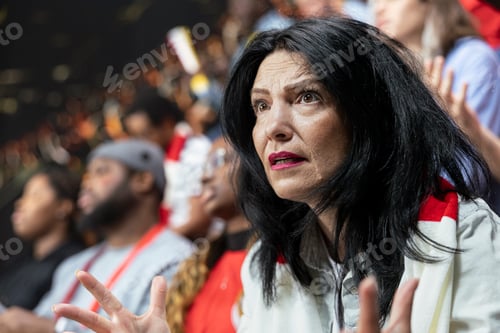 Preview: Close up of worried mature female football fan with red scarf watching match