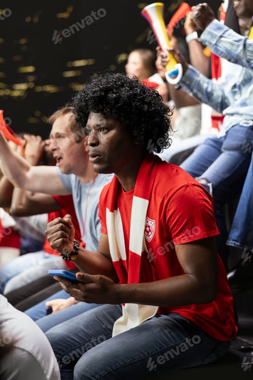 Preview: Vertical portrait of football supporter checking smartphone during tense match