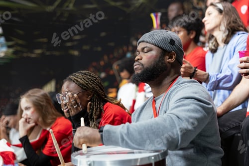 Preview: Black football supporter with drum closing eyes in stadium stands