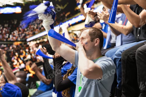 Preview: Passionate male football supporter blowing blue vuvuzela in stadium stands