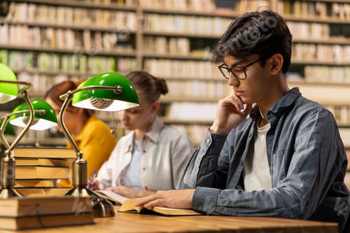 Preview: Young asian man with glasses reading book at library study table