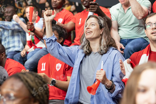 Preview: Woman football supporter cheering with red horn in red team stadium crowd