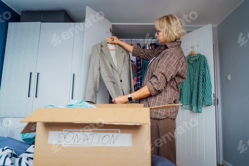 Preview: Woman putting selected clothes from her wardrobe for donating to a Charity shop. Decluttering, Sorti