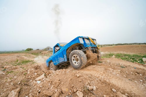 Preview: Blue off-road truck driving uphill on rugged dirt terrain