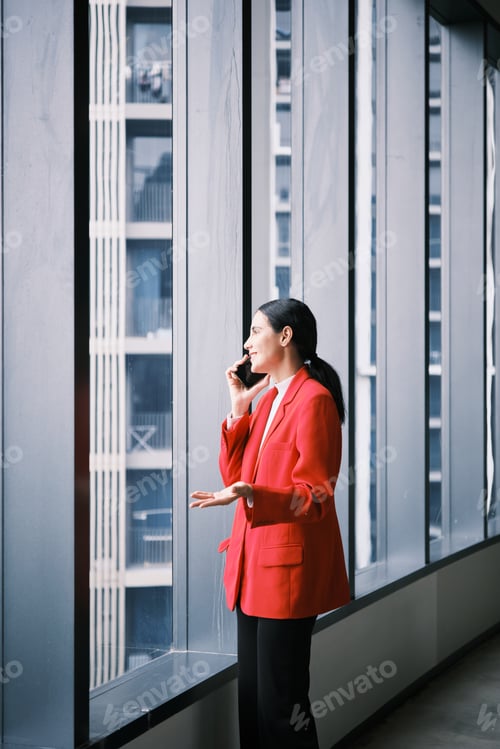 Preview: Hispanic businesswoman talking on mobile phone in modern high-rise workplace.