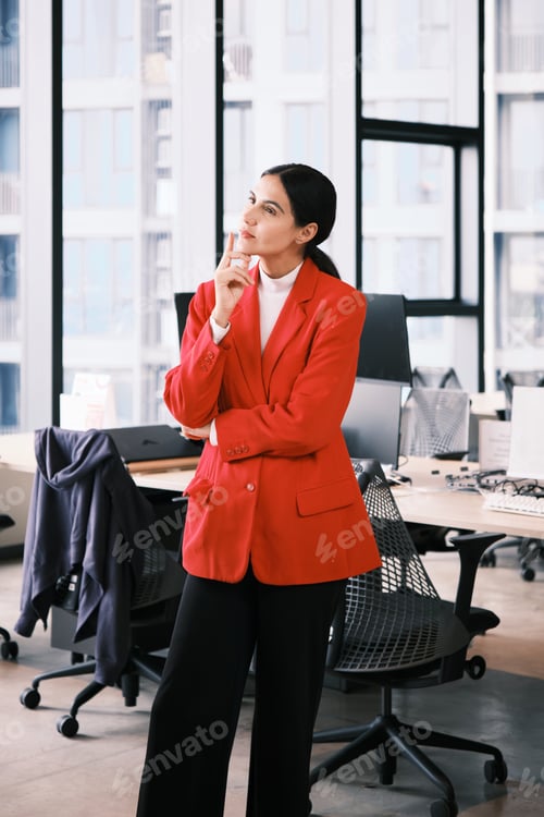 Preview: Hispanic businesswoman standing and pensive thinking in modern workplace.