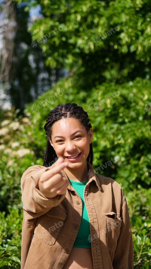 Preview: Young woman showing finger heart gesture outdoors