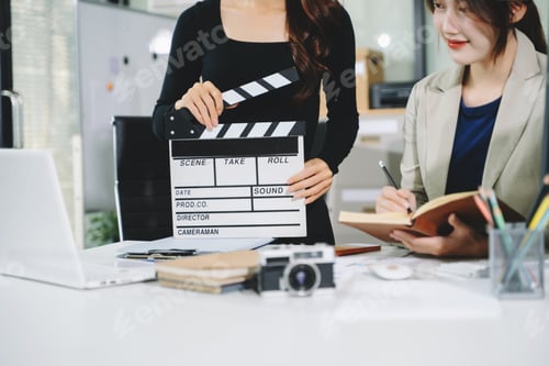 Preview: Creative team planning video production in modern office, using clapperboard, laptop and notebook. B