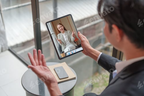 Preview: Asian man on video call waving at tablet for online business meeting