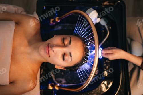 Preview: Overhead view of woman receiving head spa treatment with circular device and water