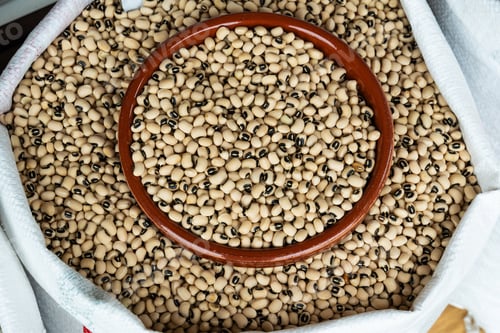 Preview: Dried black-eyed peas filling a ceramic bowl inside a large burlap sack at a market
