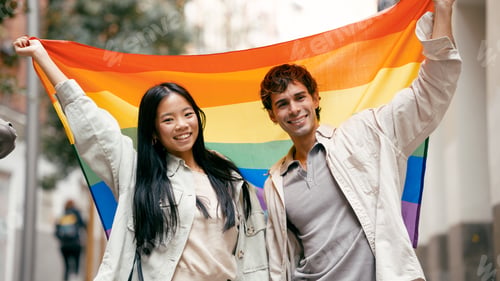 Preview: Diverse couple holding rainbow flag celebrating pride outdoors
