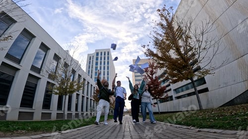 Preview: Students celebrating graduation on university campus throwing papers