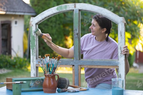 Preview: Womanpainting a wooden furniture outdoors, an eco-friendly re-use business.