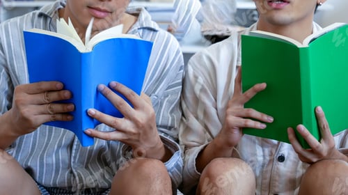 Preview: Asian two man holding book reading magazine together living room. Man relax read book happy learning