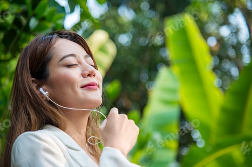 Preview: Happy asian woman use headphones listen to music from smartphone outdoor in green park nature. Music