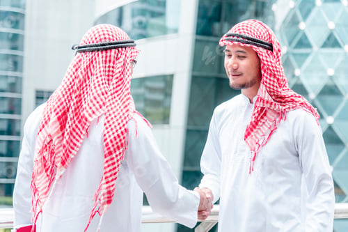 Preview: Arab Businessman Muslim dress shaking hands together in modern city UAE background. Muslim Men Teamw