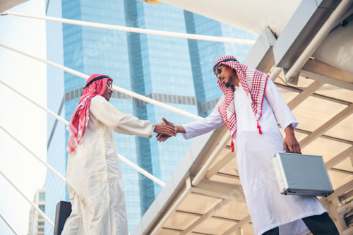 Preview: Arab Businessman Muslim dress shaking hands together in modern city UAE background. Muslim Men Teamw