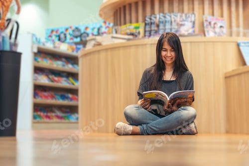 Preview: Asian woman holding book reading at bookshelf in university library. Young woman relaxation read ope
