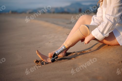 Preview: Woman with prosthetic leg relaxing on beach sand