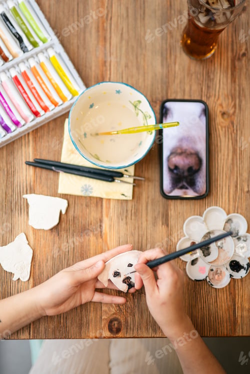 Preview: Hands painting clay dog figurine with colorful paints
