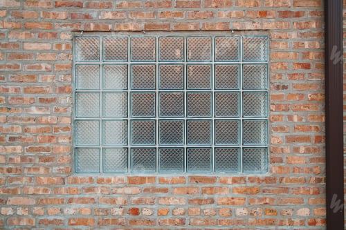 Preview: Brick wall with a large glass block window in an urban setting during bright daylight hours showing