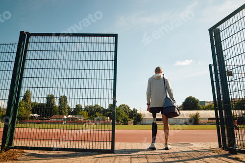 Preview: Back view of athlete with bionic leg coming to sports training at the stadium.
