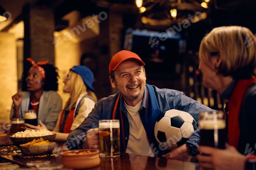Preview: Happy sports fans drinking beer and talking while watching soccer championship in a bar.