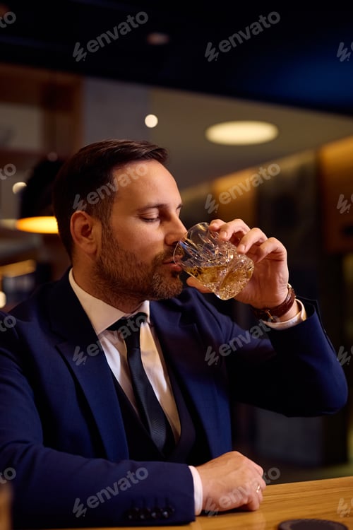 Preview: Businessman man enjoying in a glass of whiskey after work at bar counter.