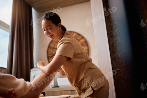 Preview: Korean massage therapist massaging man's leg with elbow during wellness treatment at the spa.
