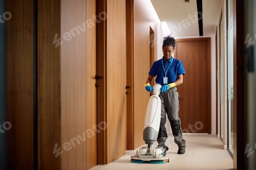 Preview: Black janitorial staff member using floor cleaning machine in corporate office corridor.