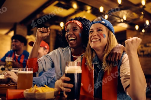 Preview: Cheerful women celebrating while watching live sports match in pub.