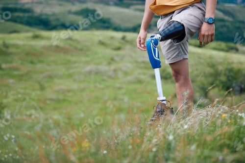 Preview: Unrecognizable man with leg disability walking through grass while hiking in nature.