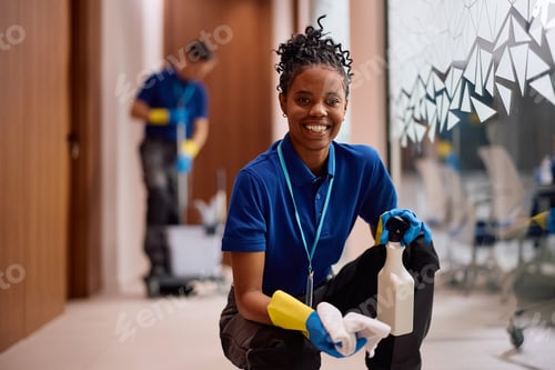Preview: Happy female janitorial staff member cleaning glass panels in the office and looking at camera.