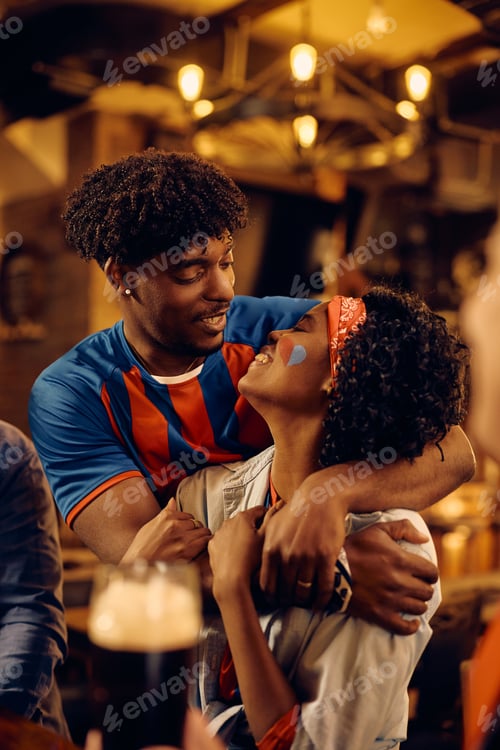 Preview: Embraced black couple enjoying in watching sports championship in a pub.
