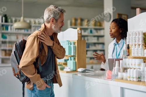 Preview: Mature man complaining of shoulder pain to his pharmacist in a pharmacy.