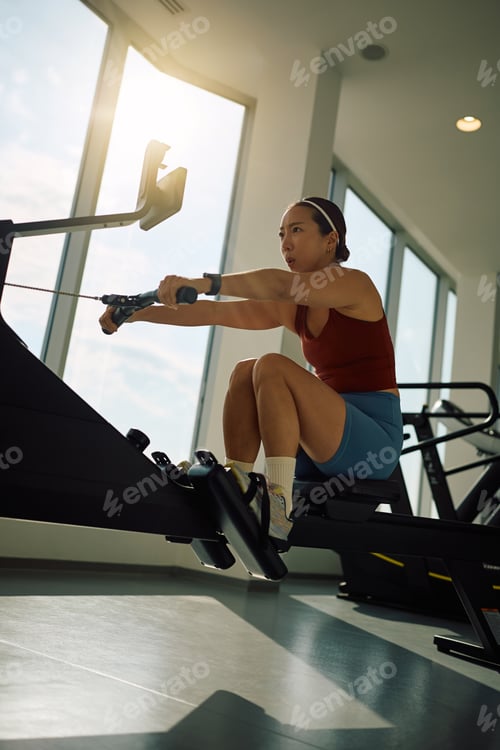 Preview: Korean athletic woman using rowing machine during sports training in a gym.