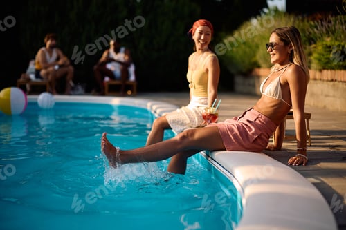 Preview: Young happy woman relaxing with her friend by swimming pool in summer day.