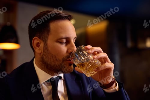Preview: Smiling businessman drinking whiskey in a bar.