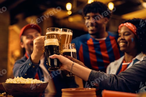 Preview: Close up of sports fans toasting with beer in a bar.