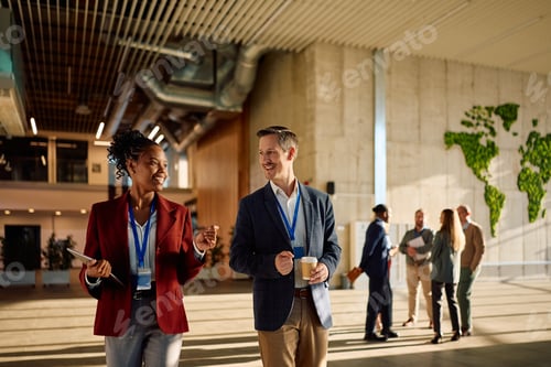 Preview: Happy business colleagues talking during conference break in hallway of an office building.