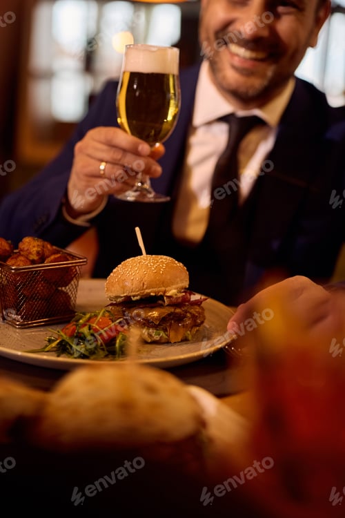 Preview: Close up of man drinking beer while having dinner in burger bar.